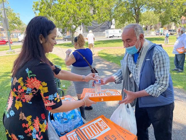 A volunteer hands over water and a meal box in summer