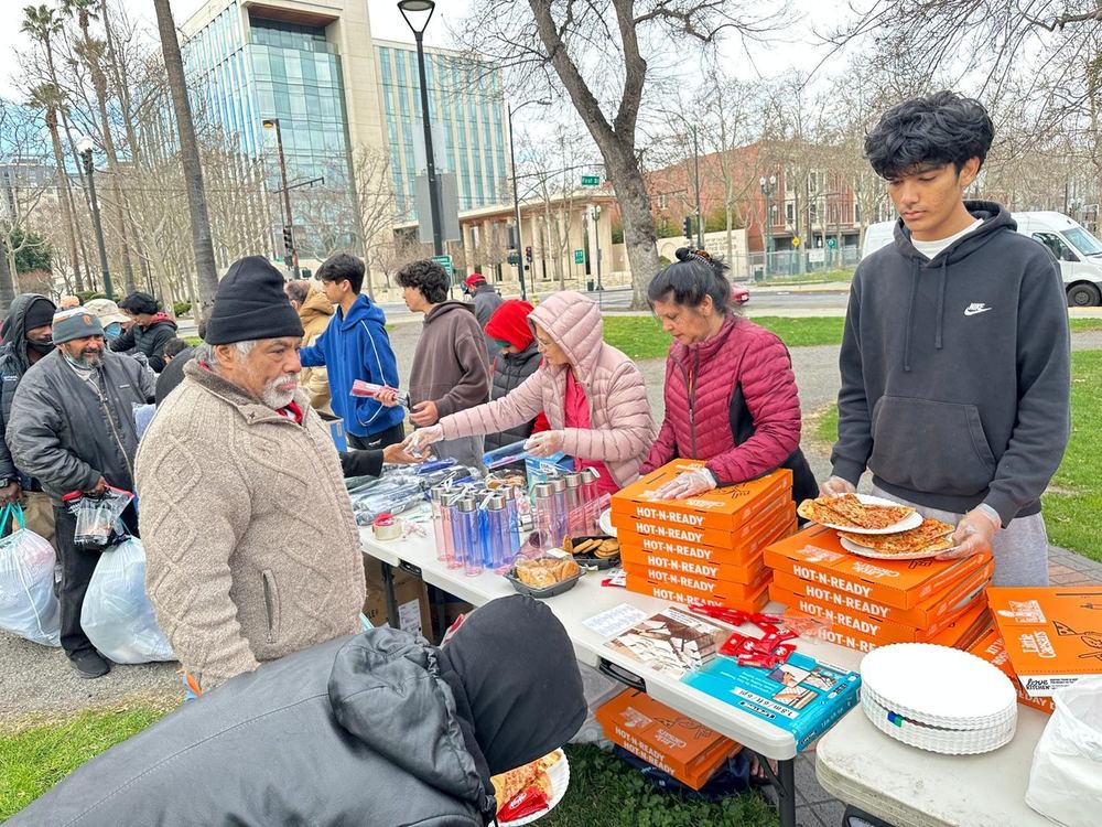Volunteers serving pizza, drinks and supplies from folding tables in the park